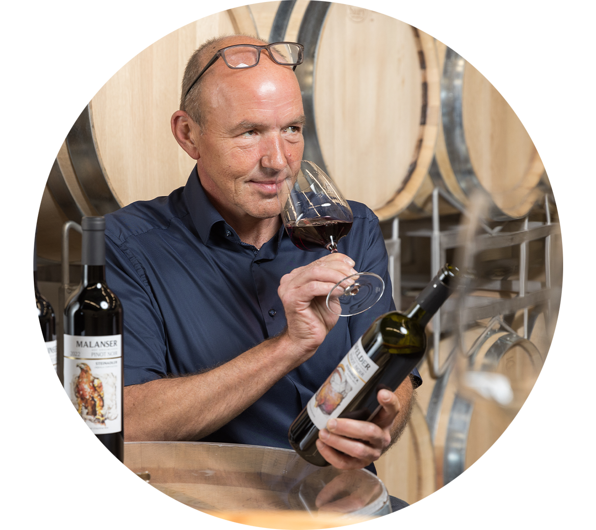 Konzentriert überprüft ein Mitarbeiter den Geruch eines Glases Rotwein. Im Hintergrund sind Holzfässer zu erkennen.